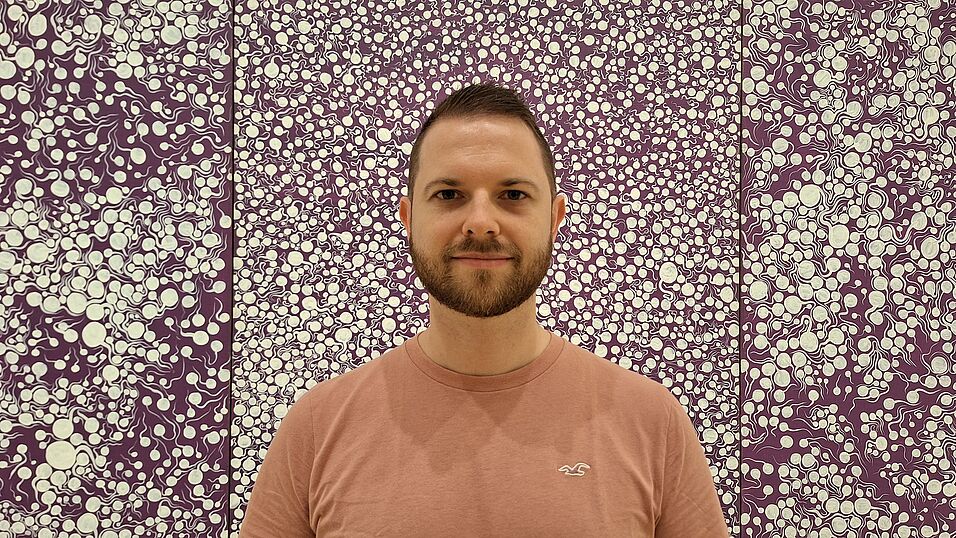 Damian Sobota, PhD (c) private; head with short brown hair and a beard. Light brown t-shirt in front of a a purple and white wallpaper