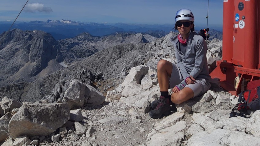 a woman with brown hair and sunglasses is sitting on the top of a mountain