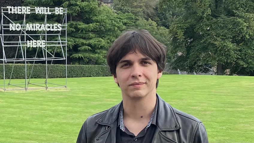 head of a ma, brown hair, background meadow with a sign There will be no miricales here